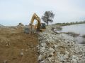 Construction excavator picking up dirt next to dam