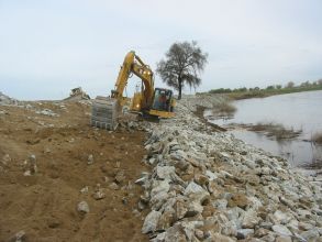 Construction excavator picking up dirt next to dam